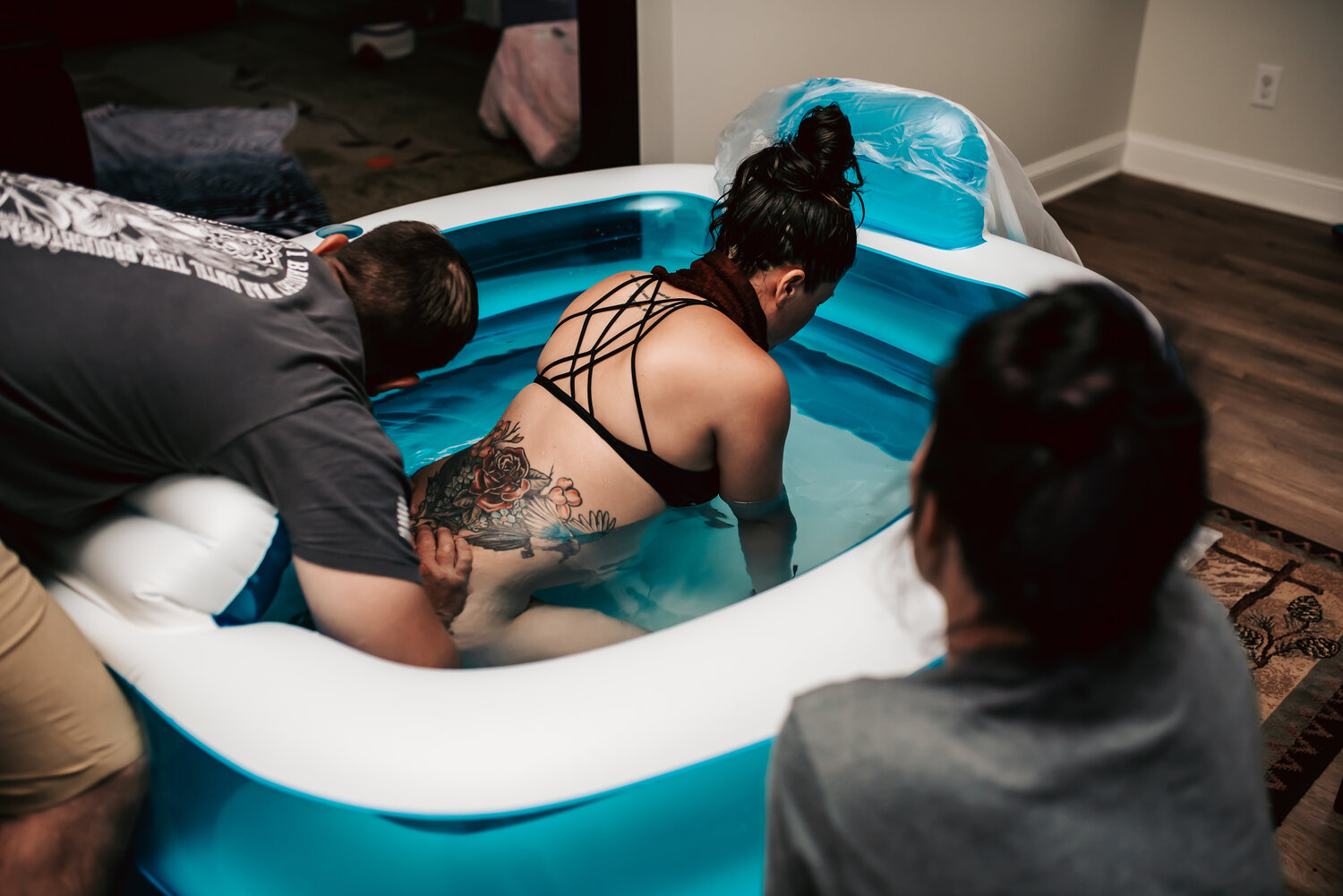Woman laboring in a birth tub during a home birth, with her husband applying counterpressure on her hips.
